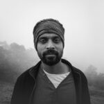Black and white portrait of a man with a beard and bandana in misty outdoor setting.